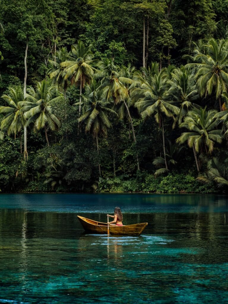 Woman paddling a wooden canoe across the clear water of Paisu Pok Lake, surrounded by forest.