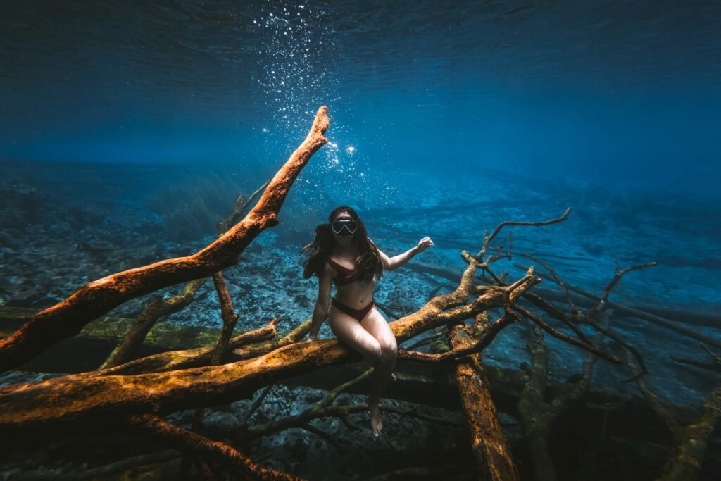 Woman sitting on sunken tree trunks underwater at Paisu Pok Lake, known for its clear water
