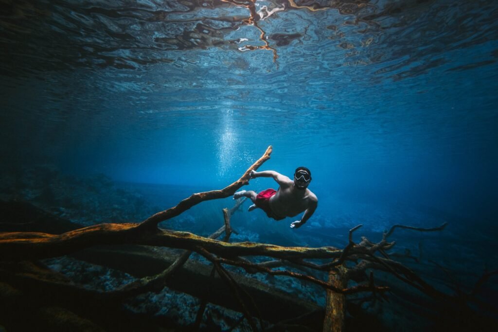 Man snorkelling over submerged tree branches in the bright blue water of Paisu Pok Lake, Banggai.